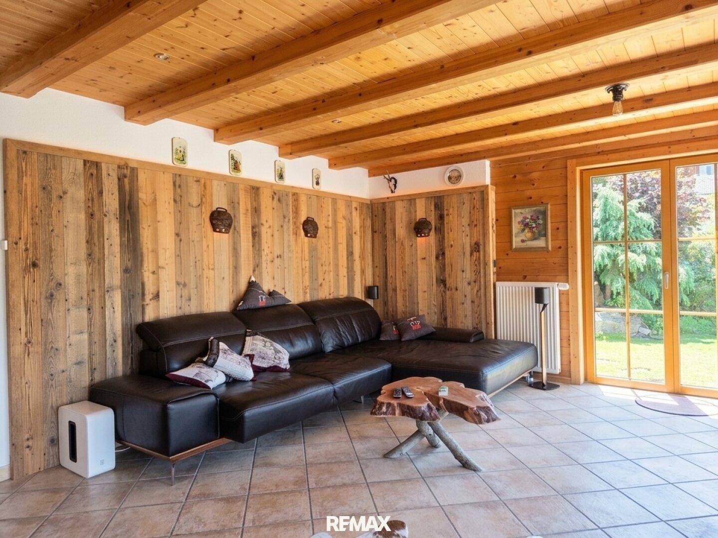 Gemütliches Wohnzimmer im alpinen Stil mit Holzwänden, Holzbalkendecke und großem Ledersofa.
