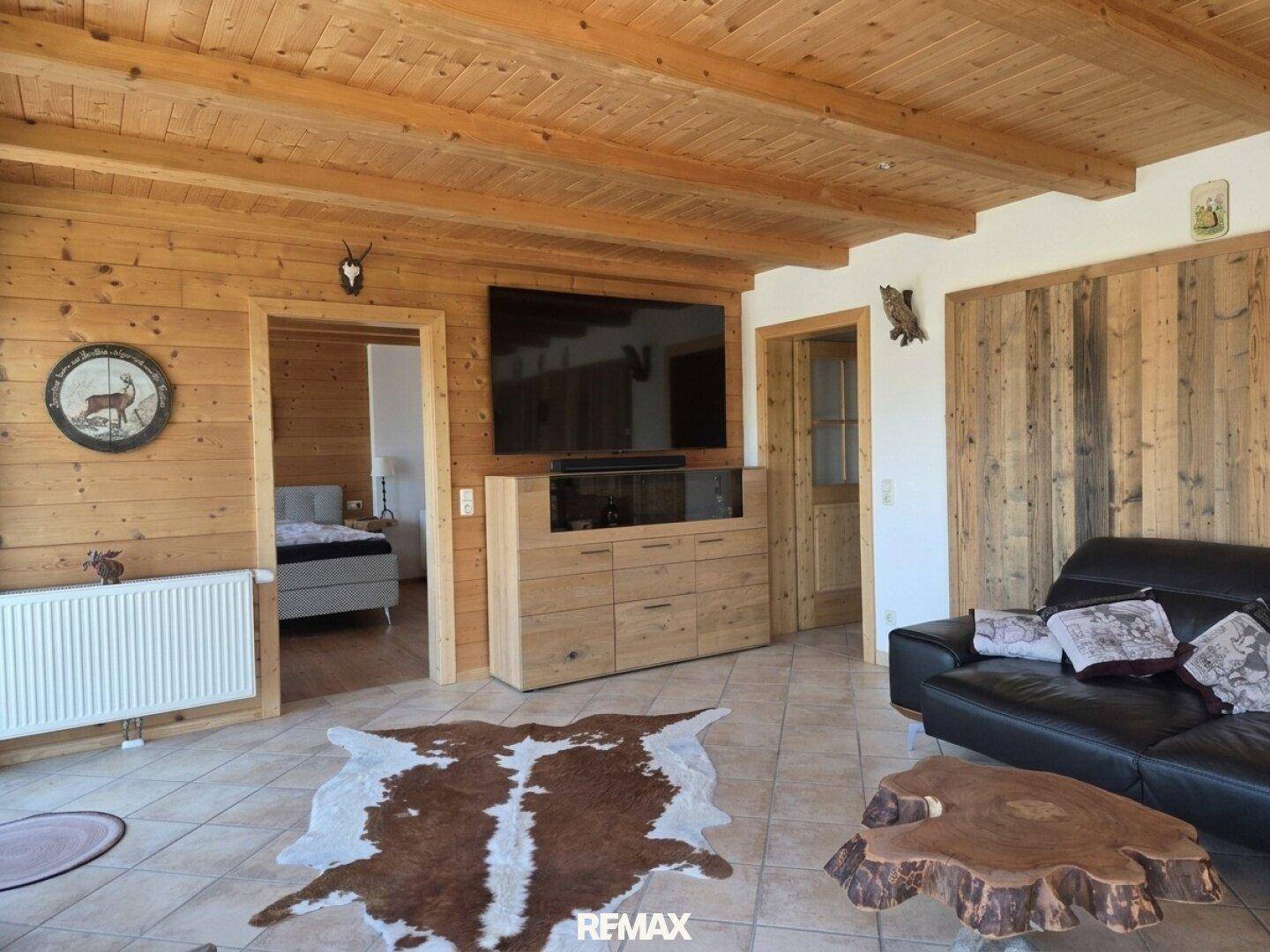Rustikales Wohnzimmer mit Holzwänden, Holzbalkendecke, großem Fernseher und traditionellen Dekorationen.