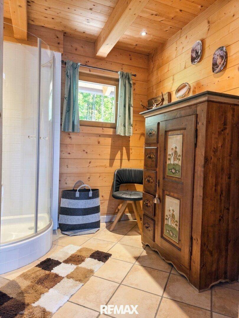 Rustikales Badezimmer mit Duschkabine, Holzwänden, Fliesenboden und einem traditionellen Holzschrank.