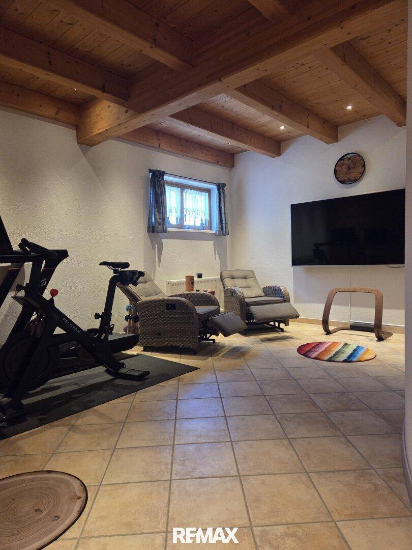 Entspannungs- und Fitnessraum mit Trainingsgerät, bequemen Sesseln und großem Flachbildfernseher.