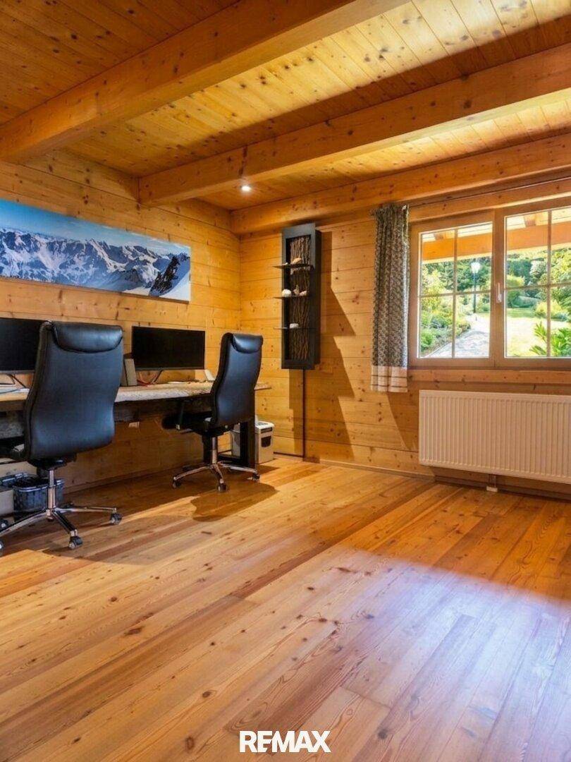 Helles Arbeitszimmer mit zwei Schreibtischen, Holzwänden, Holzboden und einem großen Fenster mit Blick ins Grüne.