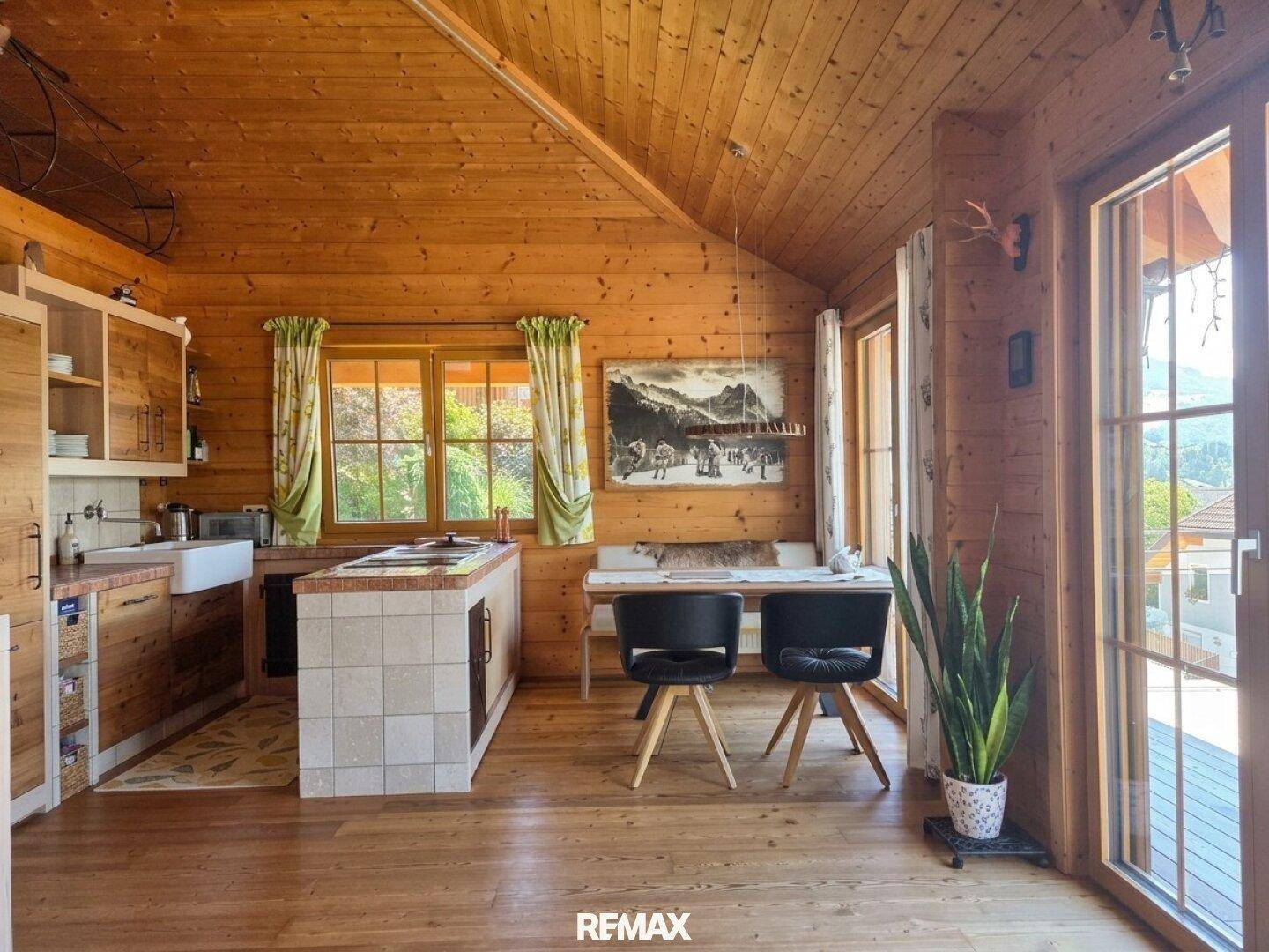 Offene Küche mit Essbereich, Holzwänden und großen Fenstern, die viel Tageslicht hereinlassen.