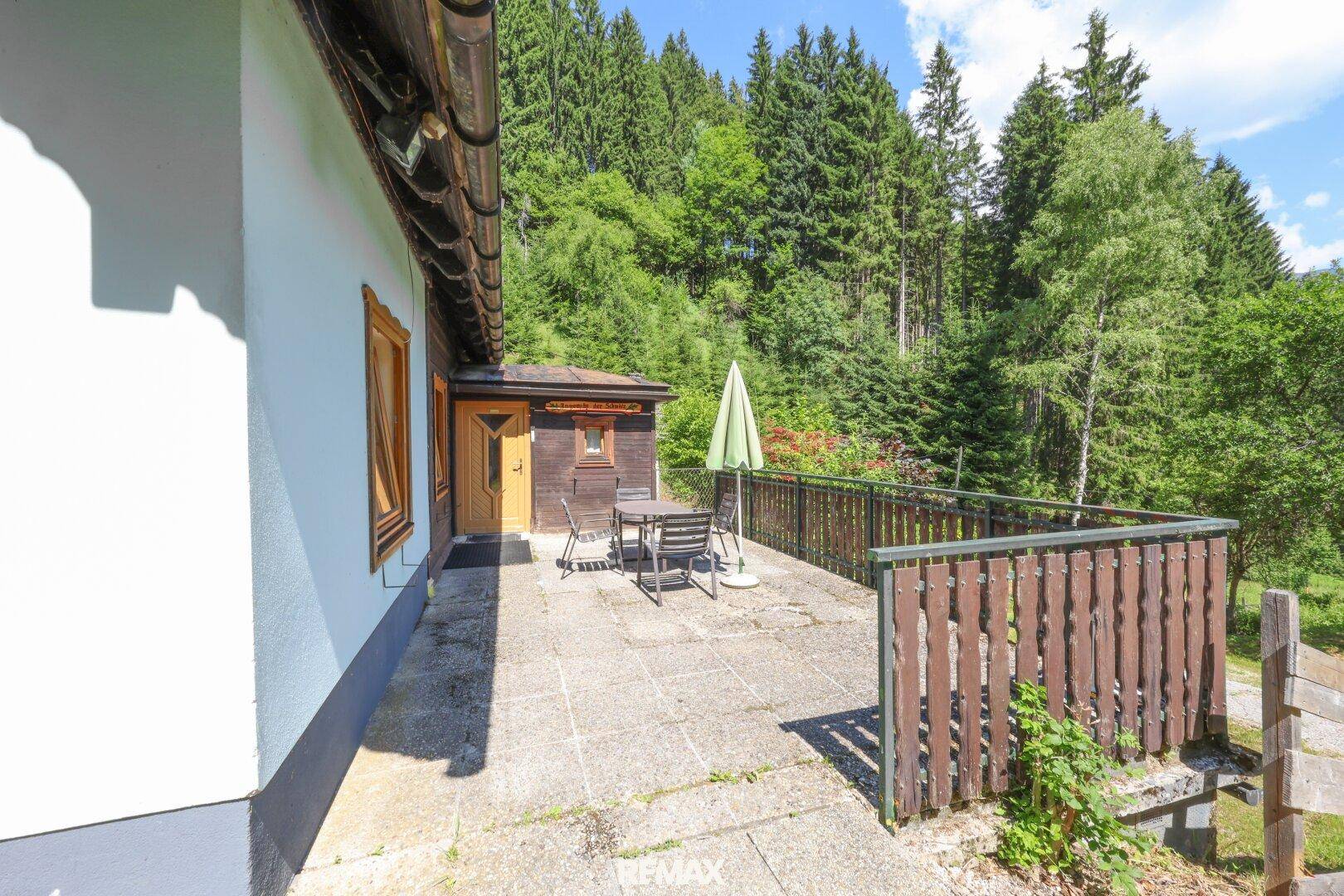Gemütliche Steinterrasse mit Gartenmöbeln und Blick auf die bewaldete Umgebung.