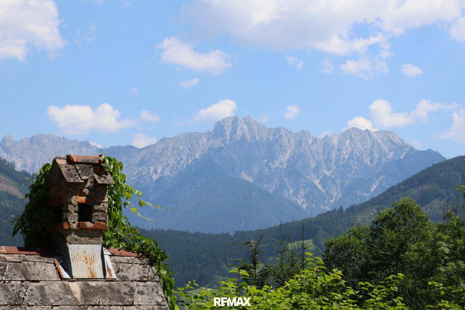 Beeindruckender Bergblick über die Dächer, mit einem alten Schornstein im Vordergrund.