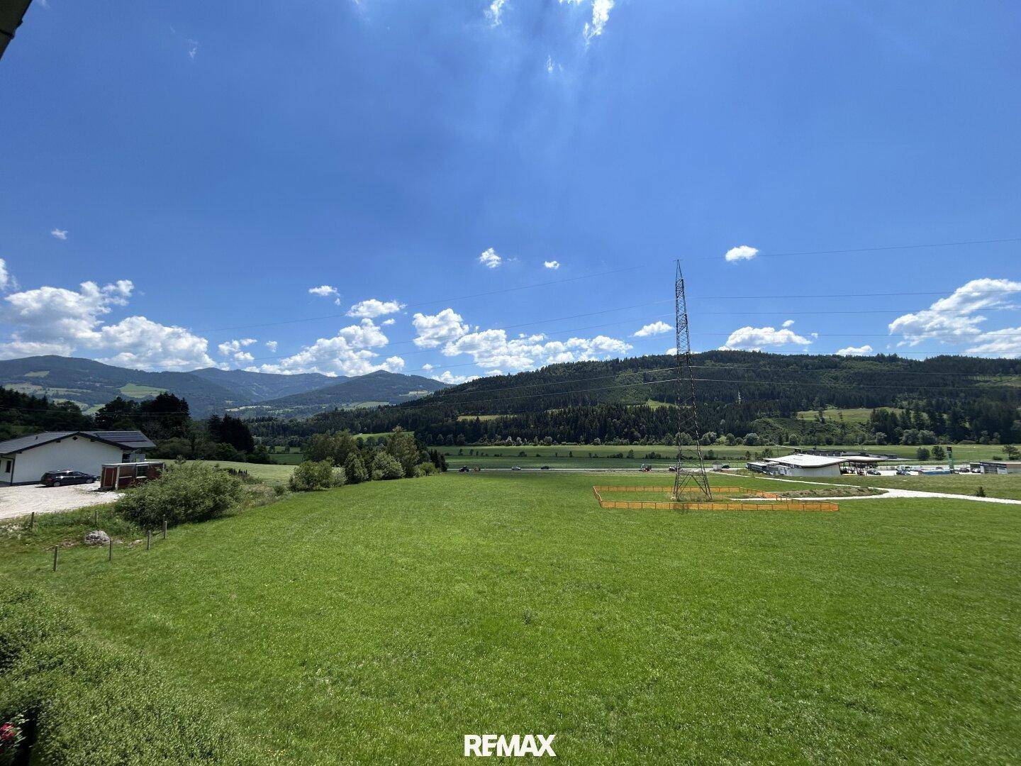 Weitläufiger Panoramablick über grüne Wiesen und bewaldete Hügel unter blauem Himmel.