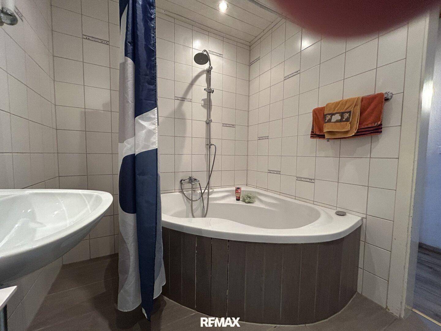 Badezimmer mit Eckbadewanne und Duschvorhang, gefliesten Wänden und Deckenverkleidung.