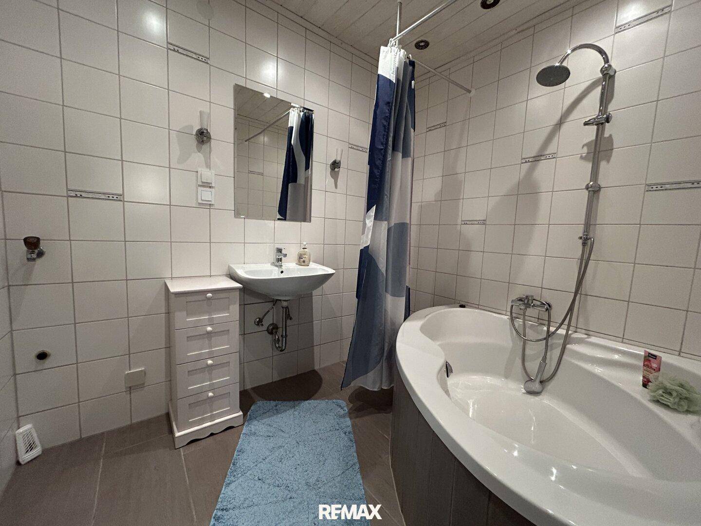 Badezimmer mit Waschbecken, Spiegel und Eckbadewanne mit Duschfunktion.