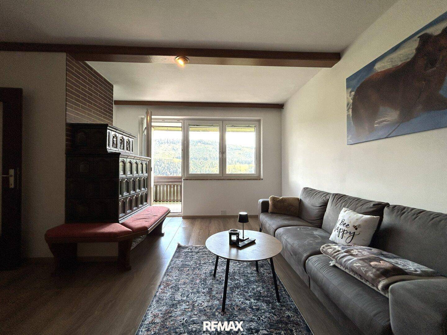 Helles Wohnzimmer mit Kachelofen, Holzbalken und Zugang zum Balkon.