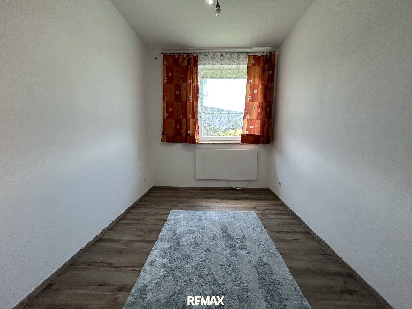 Helles Schlafzimmer mit Laminatboden, weiß gestrichenen Wänden und Fenster.