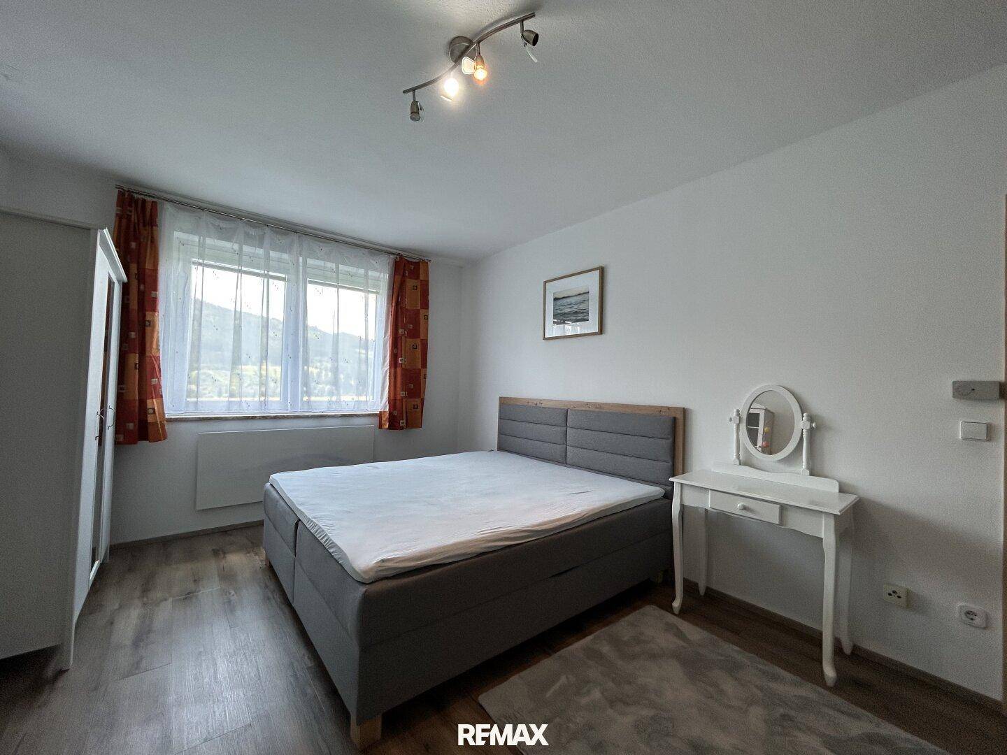 Helles Schlafzimmer mit Doppelbett, weißen Möbeln und Blick auf die Berge.