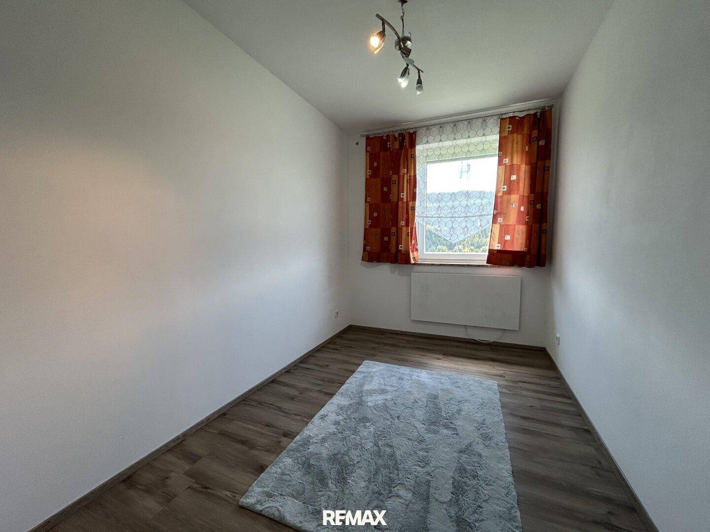 Schlafzimmer mit Laminatboden, weiß gestrichenen Wänden und Blick ins Grüne.