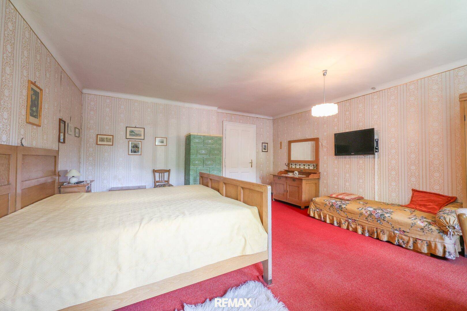 Schlafzimmer mit Doppelbett, rotem Teppichboden und traditioneller Tapete.