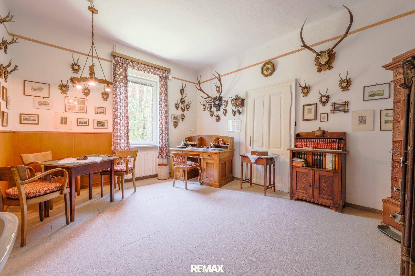 Arbeitszimmer mit traditionellen Holzmöbeln, Jagdtrophäen und hellem Teppichboden.