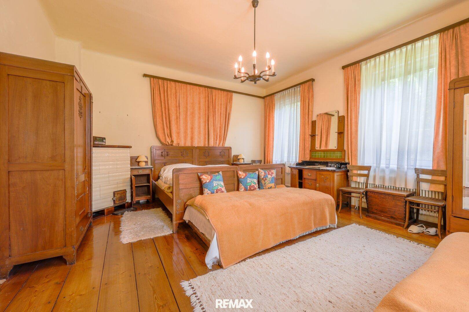 Geräumiges Schlafzimmer mit Holzboden, traditionellen Holzmöbeln und großen Fenstern.