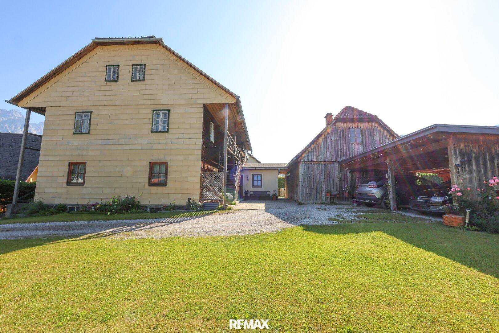 Ländliches Anwesen mit traditionellem Holzhaus, Carport und weitläufiger Grünfläche.