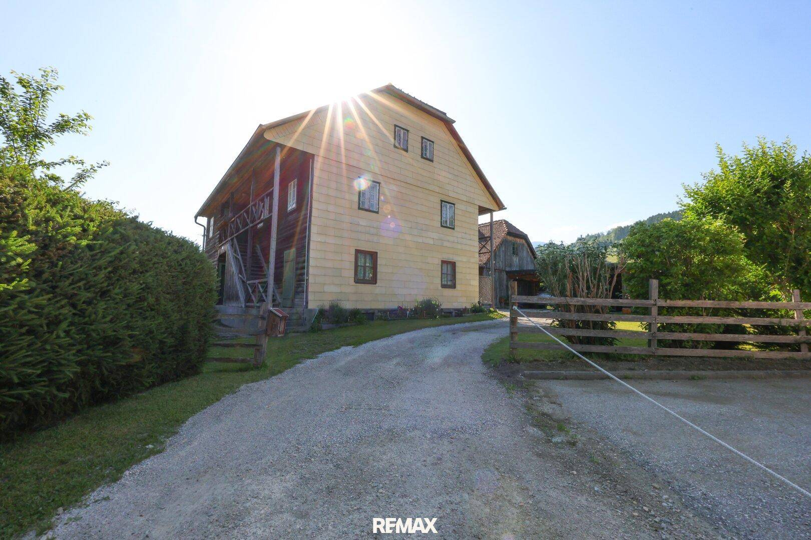 Sonniges Anwesen mit traditionellem Holzhaus, Schotterauffahrt und umzäuntem Gartenbereich.