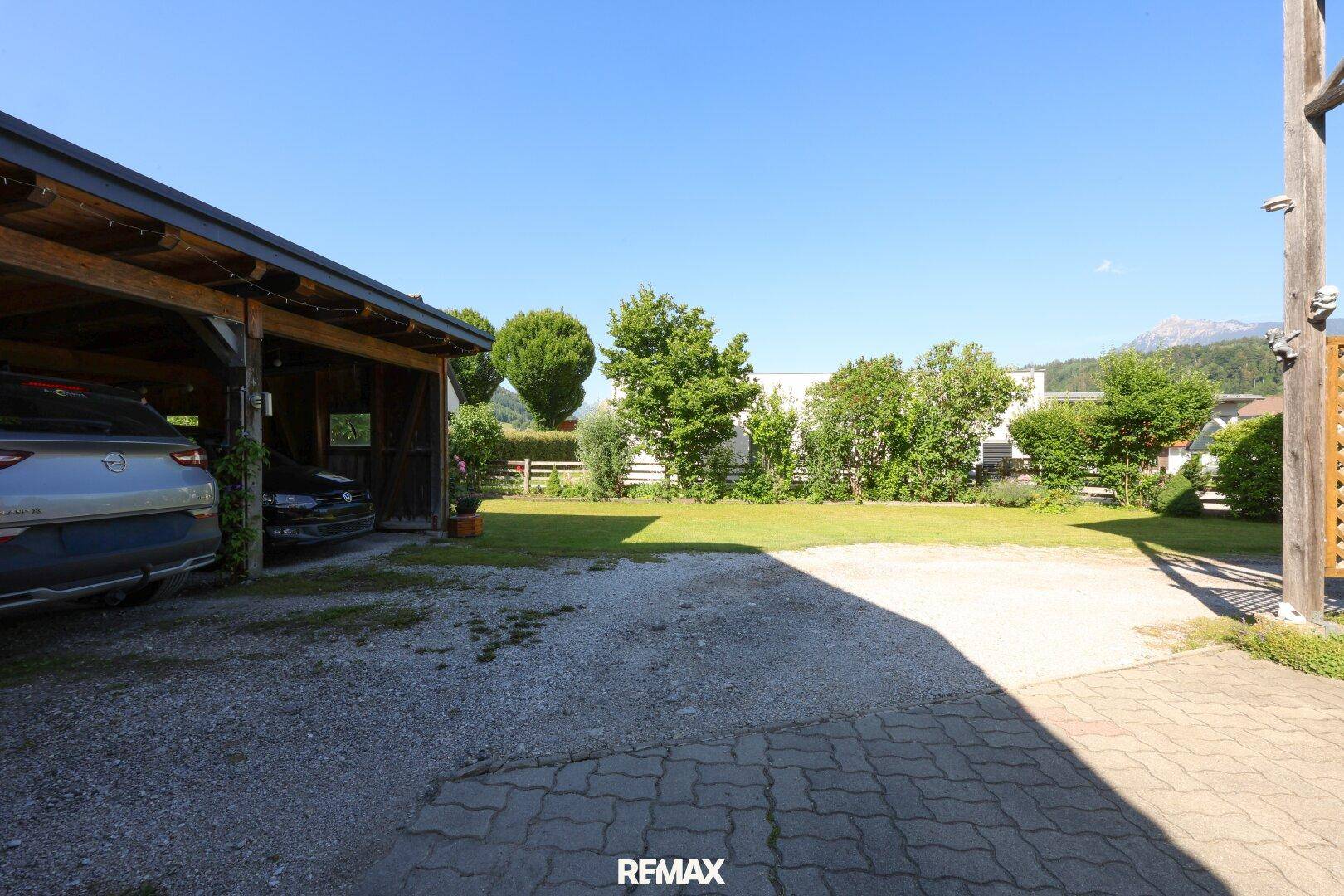 Geräumiger Außenbereich mit Carport, gepflasterter Fläche und großem Rasenbereich.