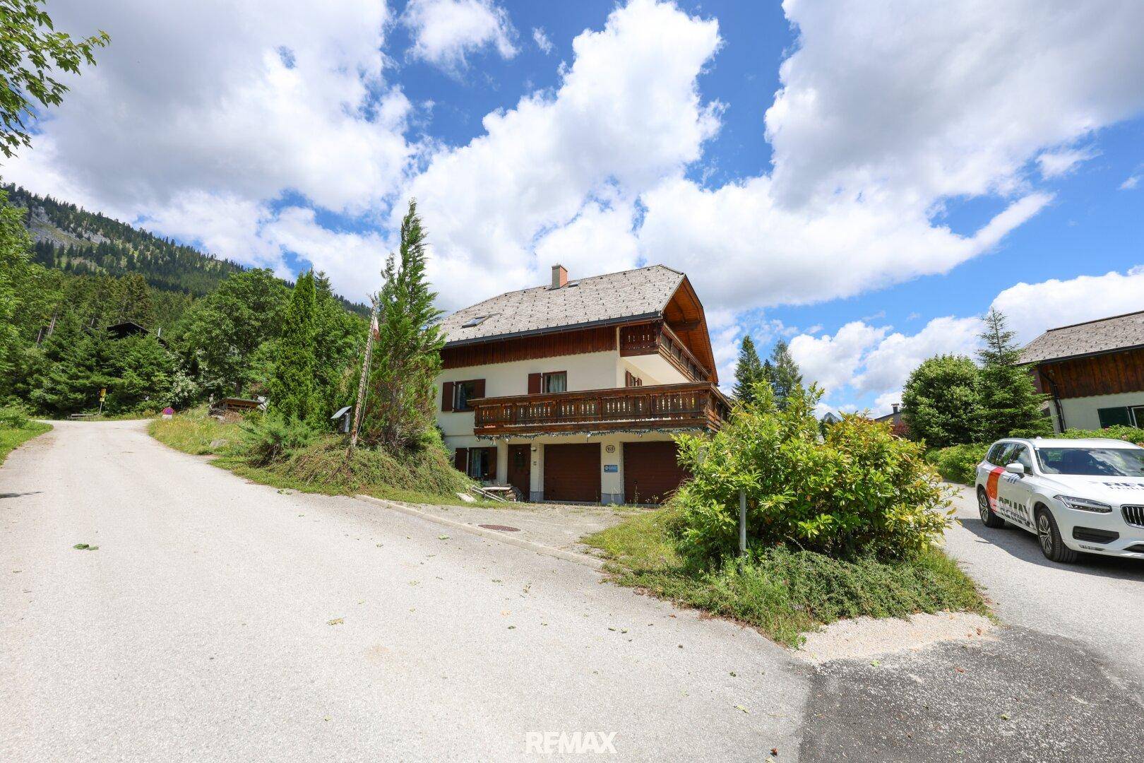 Traditionelles Haus mit Holzbalkonen und Satteldach, gelegen an einer ruhigen Straße mit Bergblick.