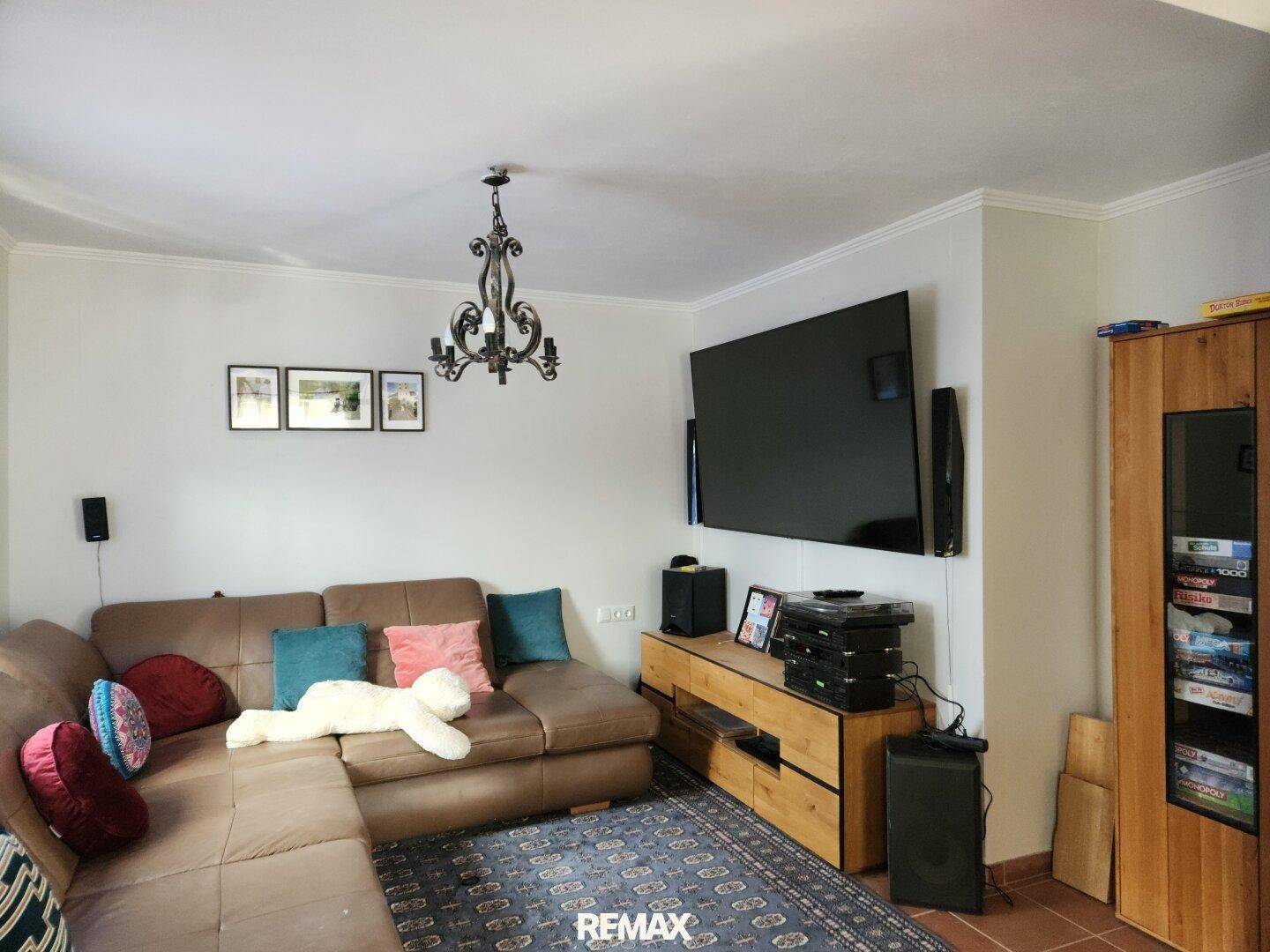 Gemütliches Wohnzimmer mit großem Ecksofa, Teppich und einem an der Wand montierten Fernseher.