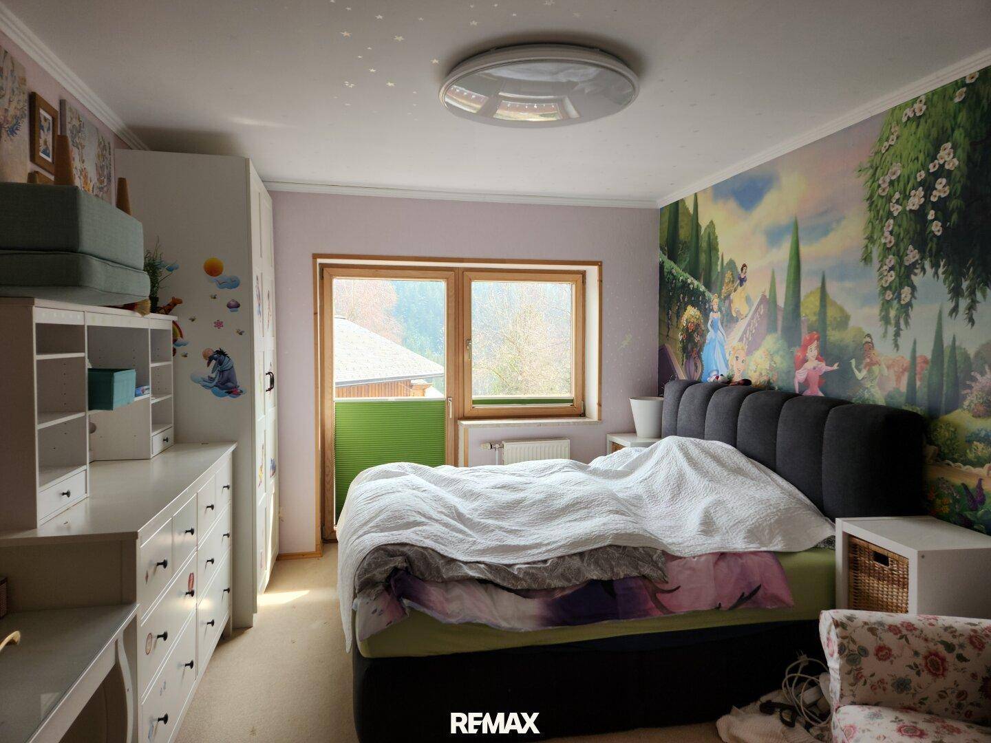 Kinderzimmer mit farbenfroher Wandtapete, Bett und einem Fenster mit Blick ins Grüne.