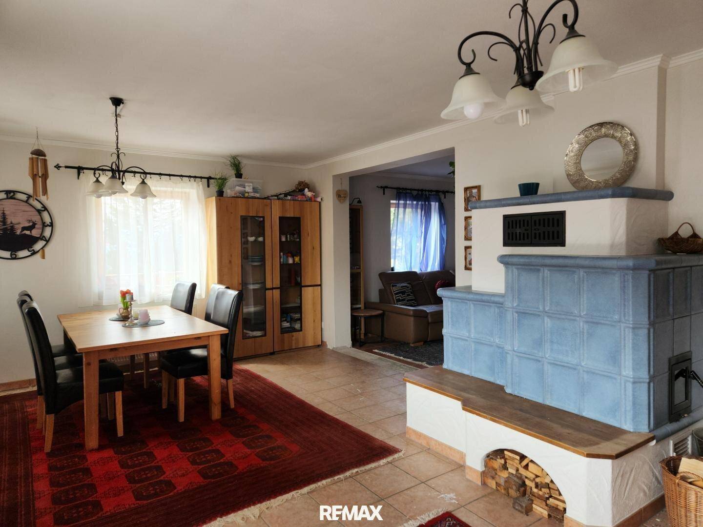 Essbereich mit Holztisch, Stühlen und einem traditionellen blauen Kachelofen als Heizelement.