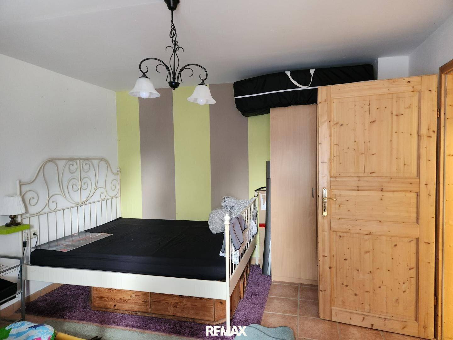 Schlafzimmer mit weißem Metallbettgestell, gestreiften Wänden und einem Kleiderschrank aus Holz.