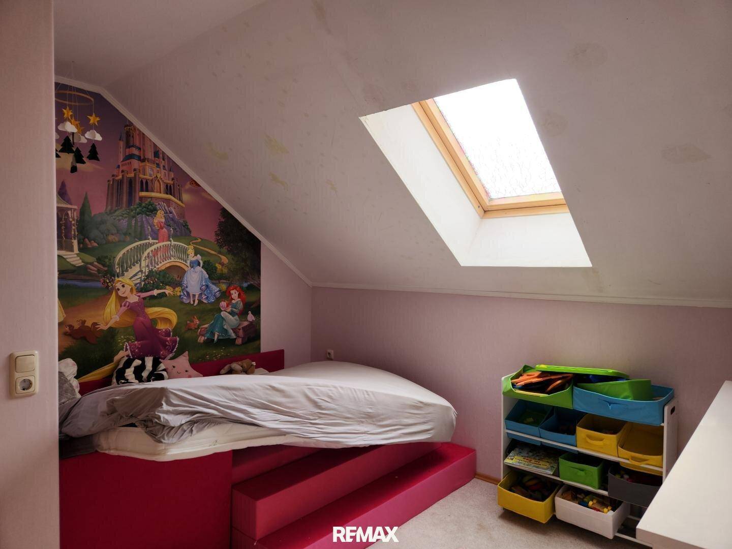 Gemütliches Kinderzimmer im Dachgeschoss mit Schrägdach, farbenfroher Tapete und Dachfenster.