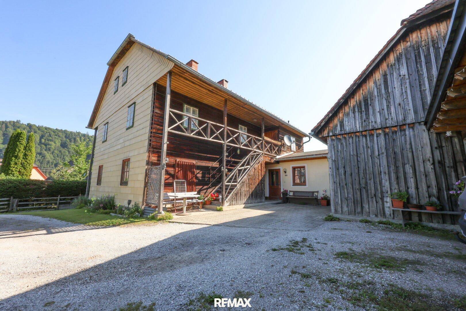 Traditionelles Holzhaus mit Außentreppe, möbliertem Innenhof und angrenzendem Nebengebäude.