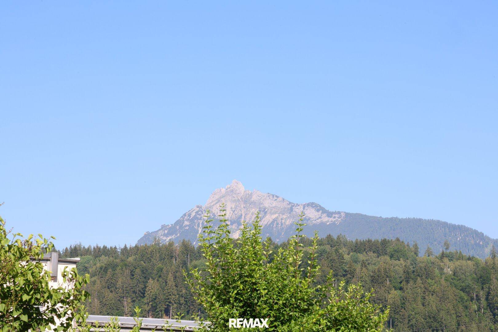 Malerischer Bergblick über grüne Baumwipfel unter strahlend blauem Himmel.