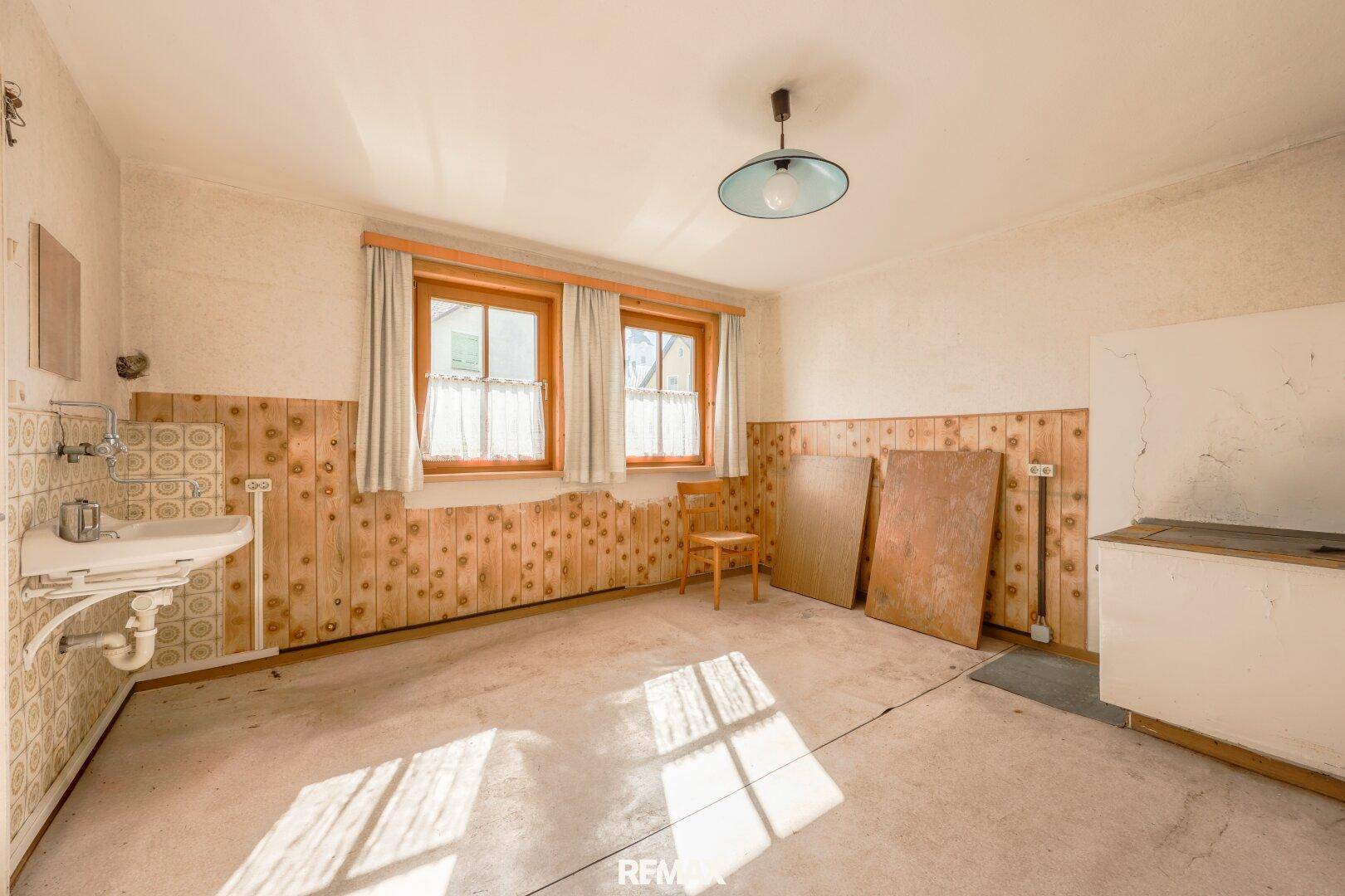 Helle Küche mit Spülbecken, Holzvertäfelung und zwei Fenstern.