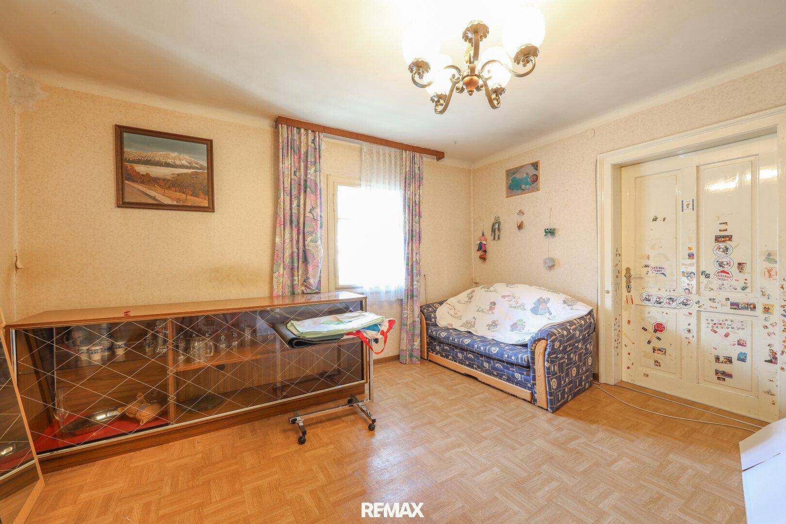 Gemütlicher Raum mit Parkettboden, traditionellem Schrank und Sofa, renovierungsbedürftig.