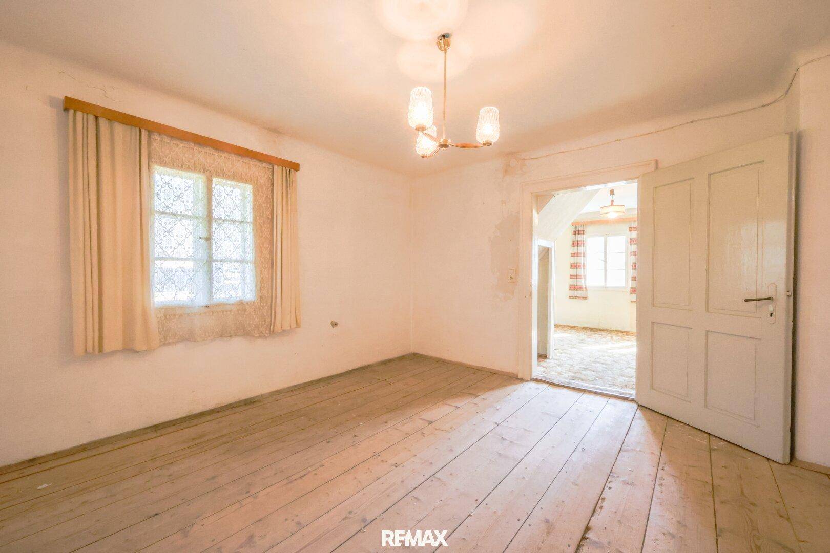 Helles Schlafzimmer mit Holzdielenboden, Fenster und Renovierungsbedarf.