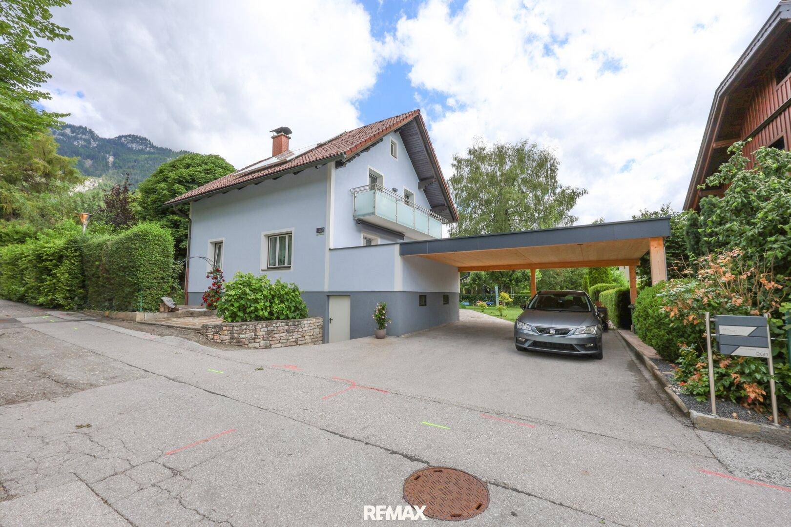 Ansicht des Hauses von der Straße mit Carport und gepflasterter Zufahrt unter bewölktem Himmel.