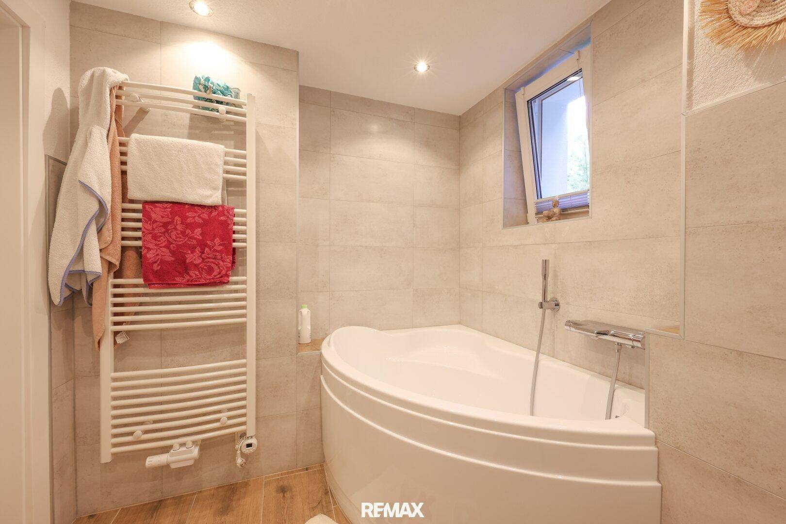 Helles Badezimmer mit Eckbadewanne, beheiztem Handtuchhalter und Fenster.