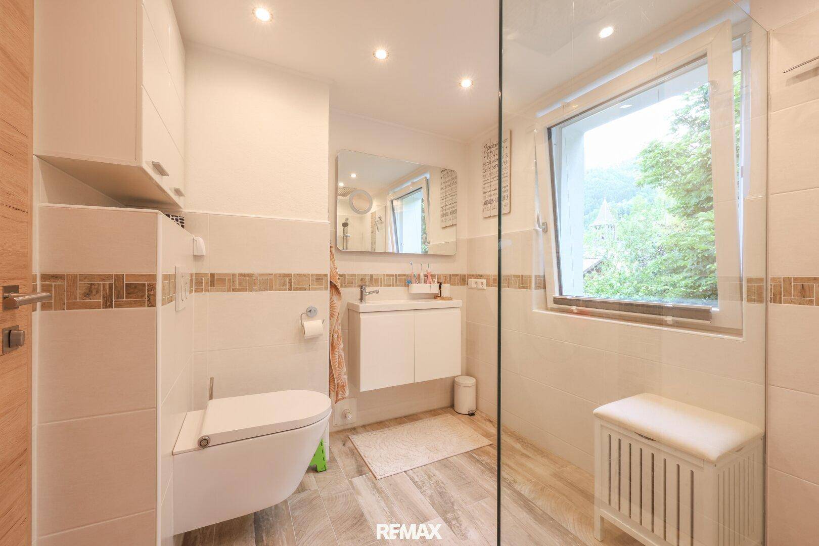 Helles Badezimmer mit Dusche, WC, Waschtisch und Fenster für natürliche Belüftung.