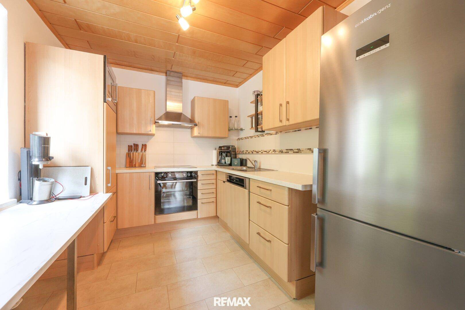 Helle Küche mit Holzdecken, hellen Holzschränken, Fliesenboden und modernen Geräten.