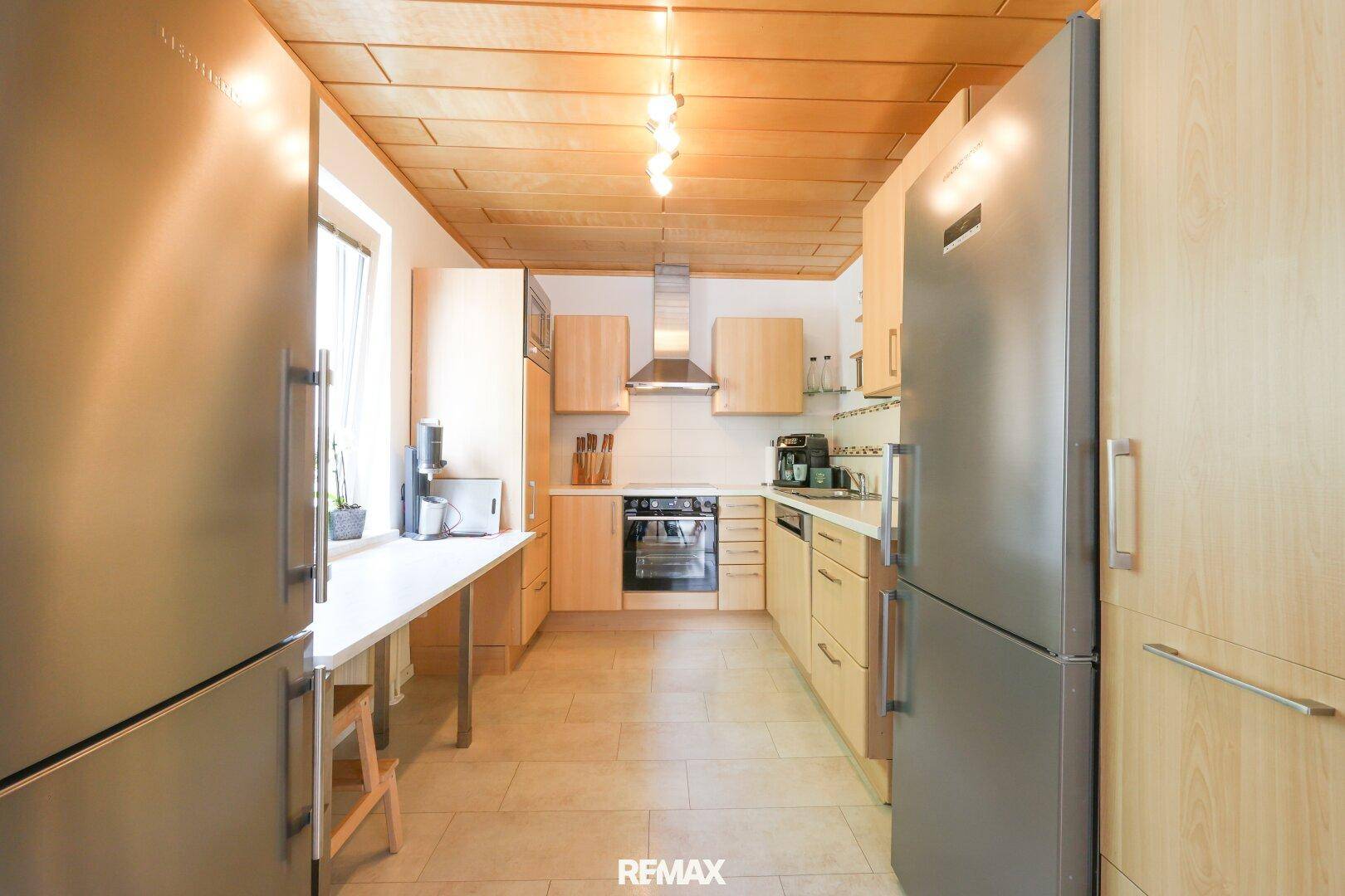 Funktionale Küche mit zwei Kühlschränken, Holzdecken und Fliesenboden.