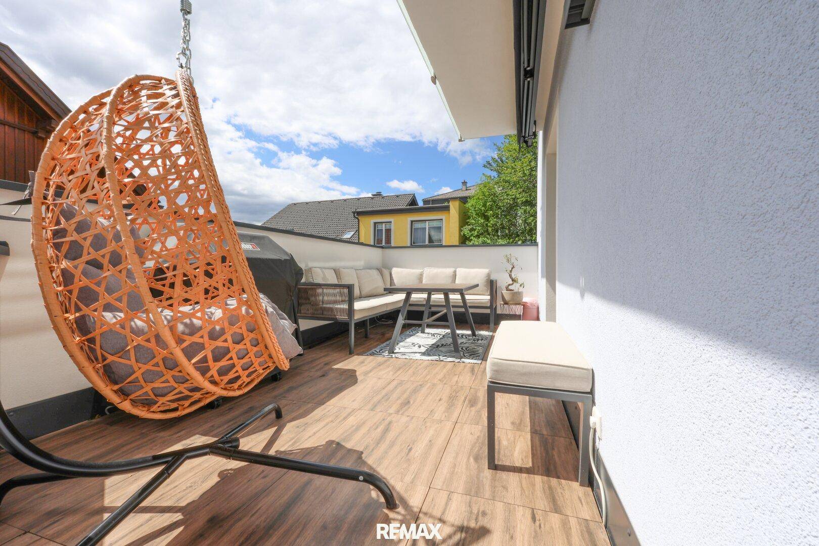 Gemütlicher Balkon mit modernen Outdoor-Möbeln, Hängesessel und Blick auf die Umgebung.