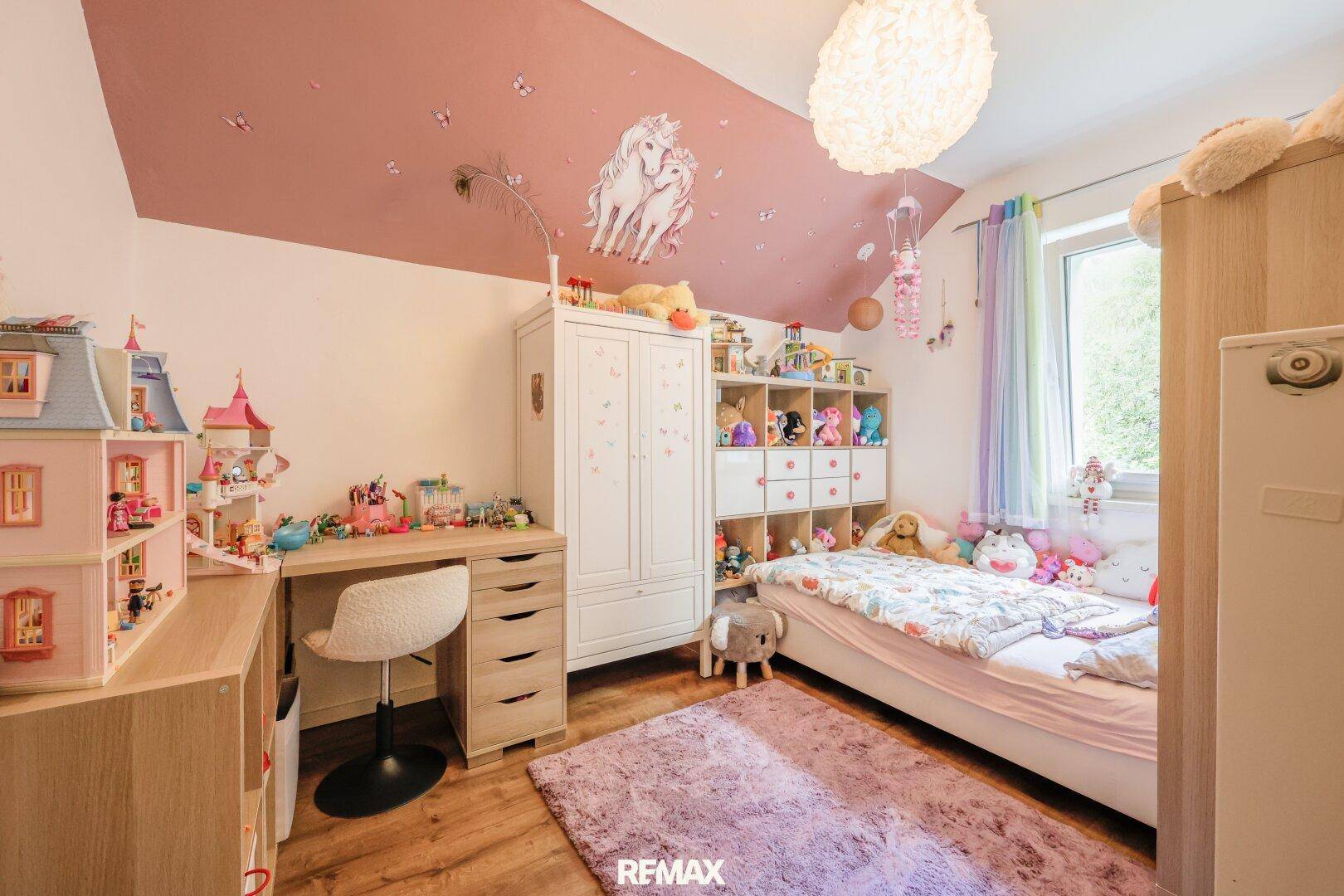 Kinderzimmer mit Schreibtisch, Bett und verspielter Dekoration an der rosa Dachschräge.