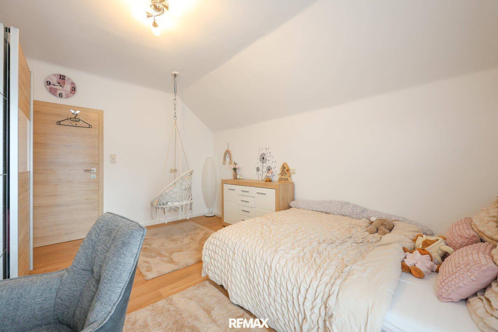 Helles Schlafzimmer mit Dachschräge, Holzboden und gemütlicher Hängeschaukel.