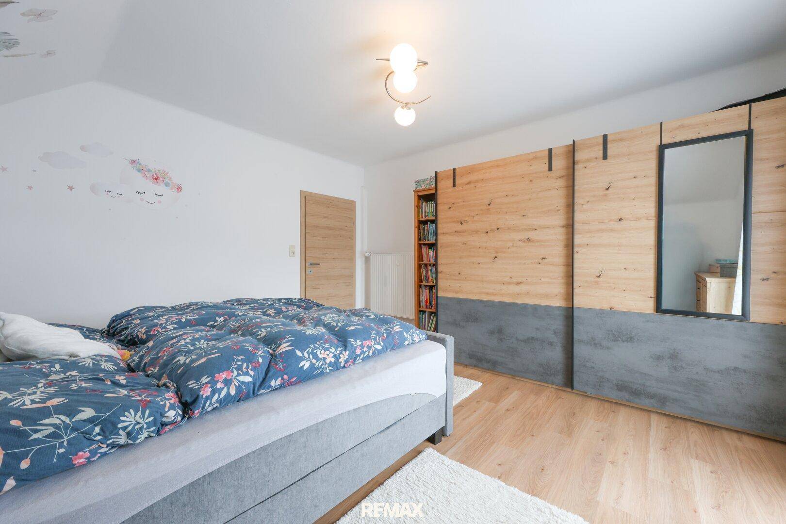 Schlafzimmer mit großem Kleiderschrank, Holzboden und floraler Wanddekoration.