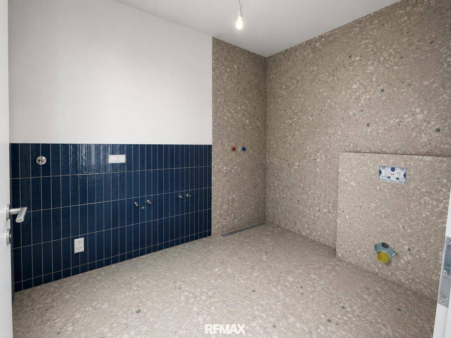 Unfertiges Badezimmer mit Fliesenboden und vorbereiteten Anschlüssen für Sanitäranlagen.