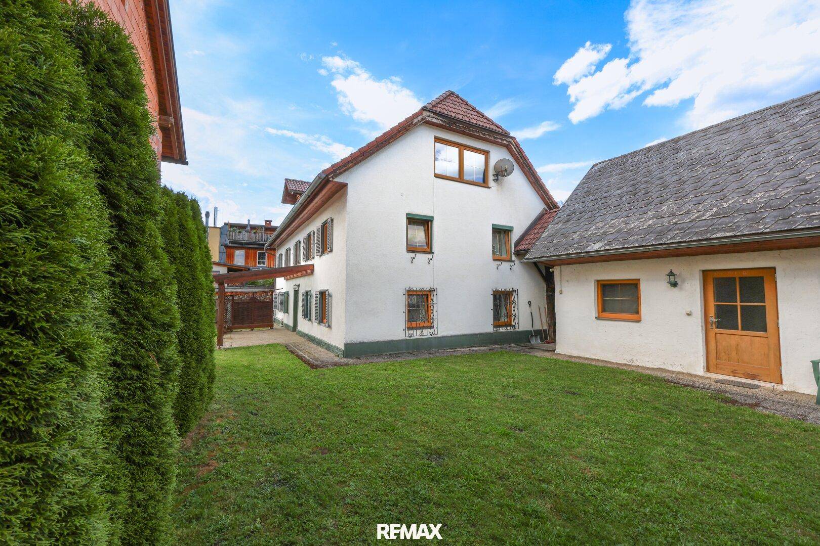 Seitenansicht des Hauses mit gepflegtem Rasen und einer hohen Hecke als Begrenzung.
