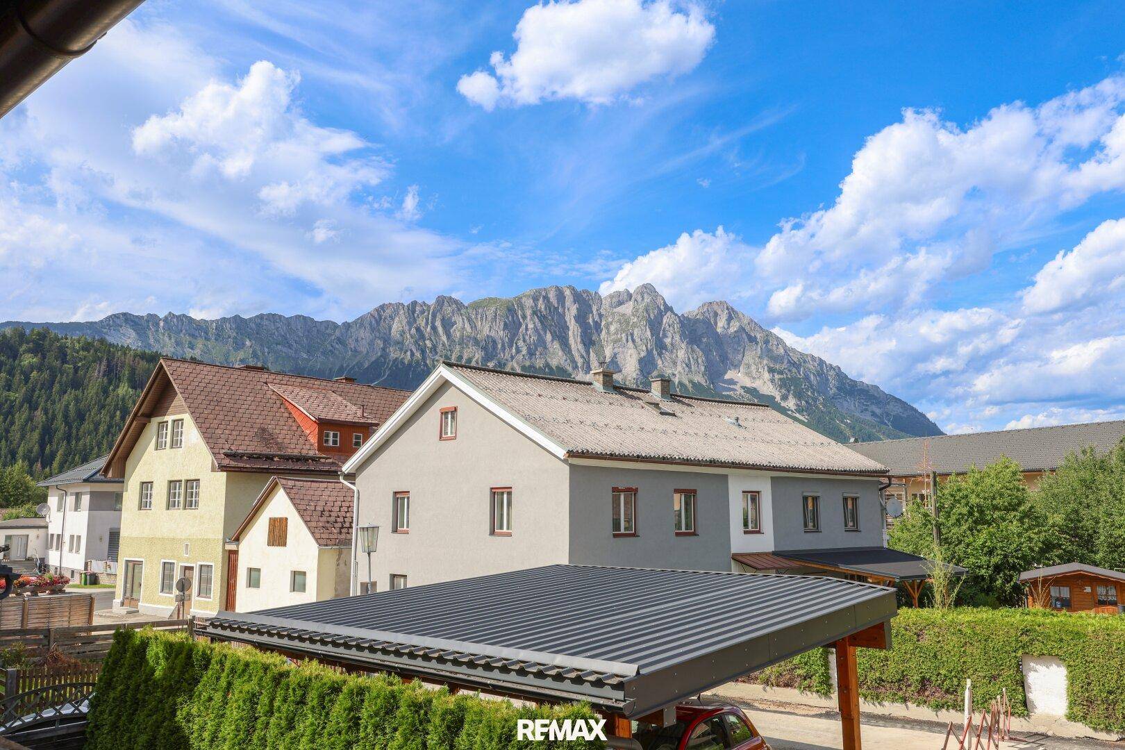 Panoramablick auf die umliegende Berglandschaft mit Wohnhäusern und einem Carport im Vordergrund.