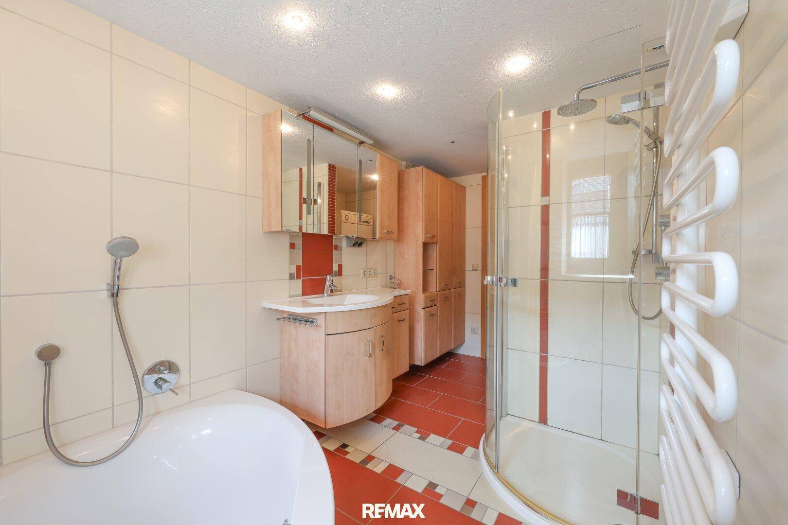 Funktionales Badezimmer mit Badewanne, Duschkabine und hellen Fliesen an Wänden und Boden.