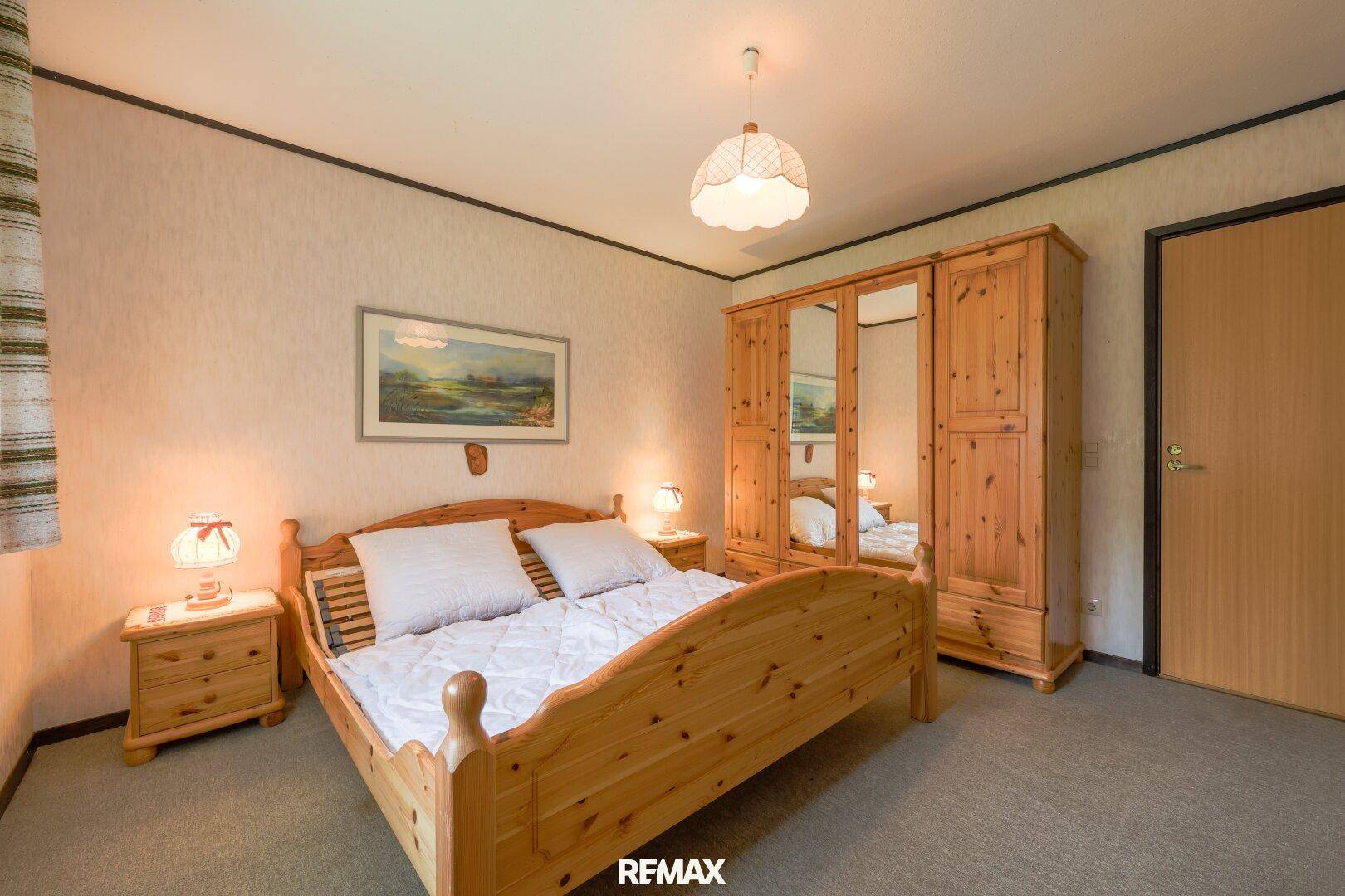 Helles Schlafzimmer mit Doppelbett aus Holz, Kleiderschrank und Teppichboden.