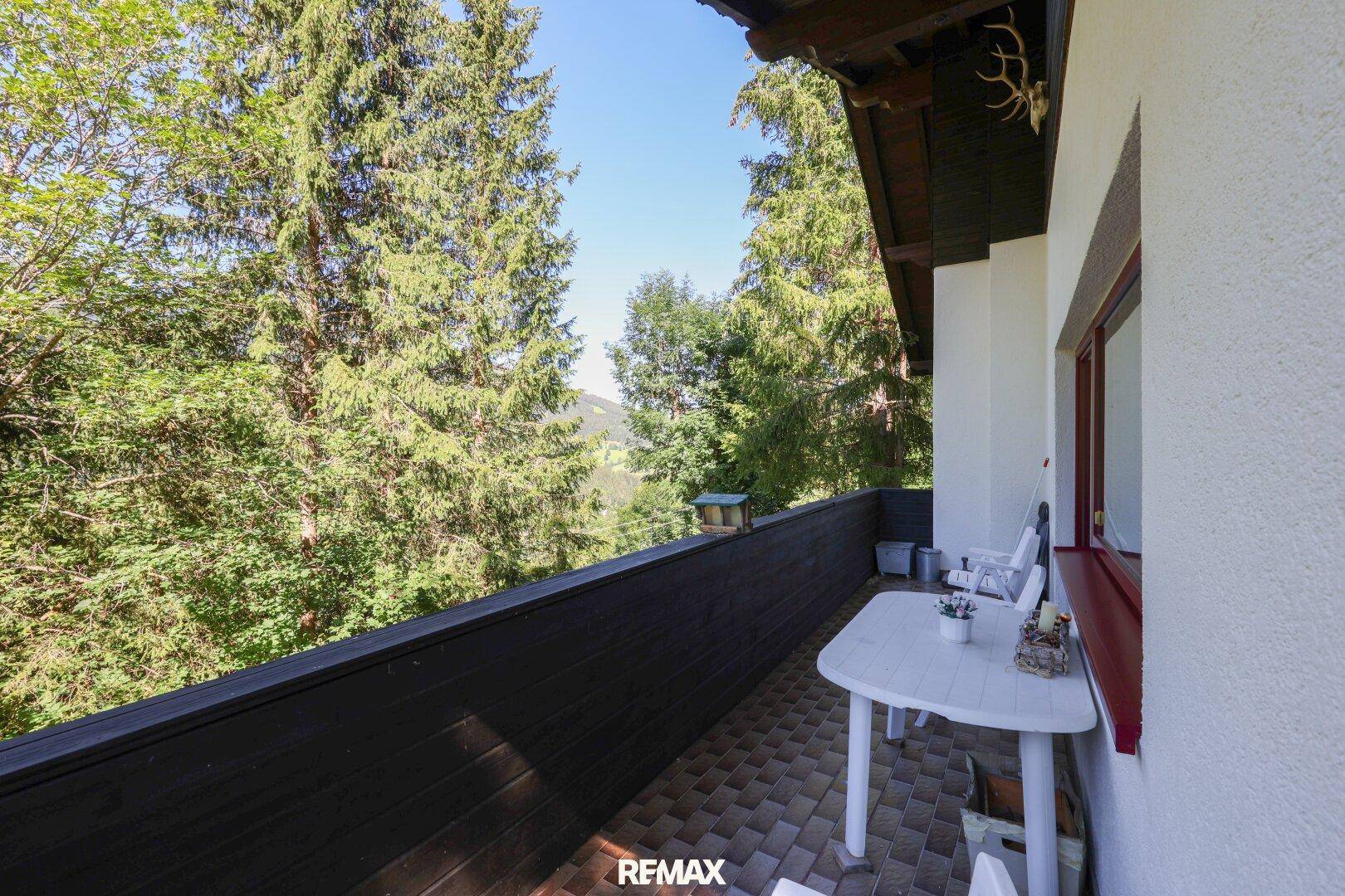Sonniger Balkon mit Holzbalken, Sitzgelegenheiten und traditionellem Hirschgeweih-Dekor.