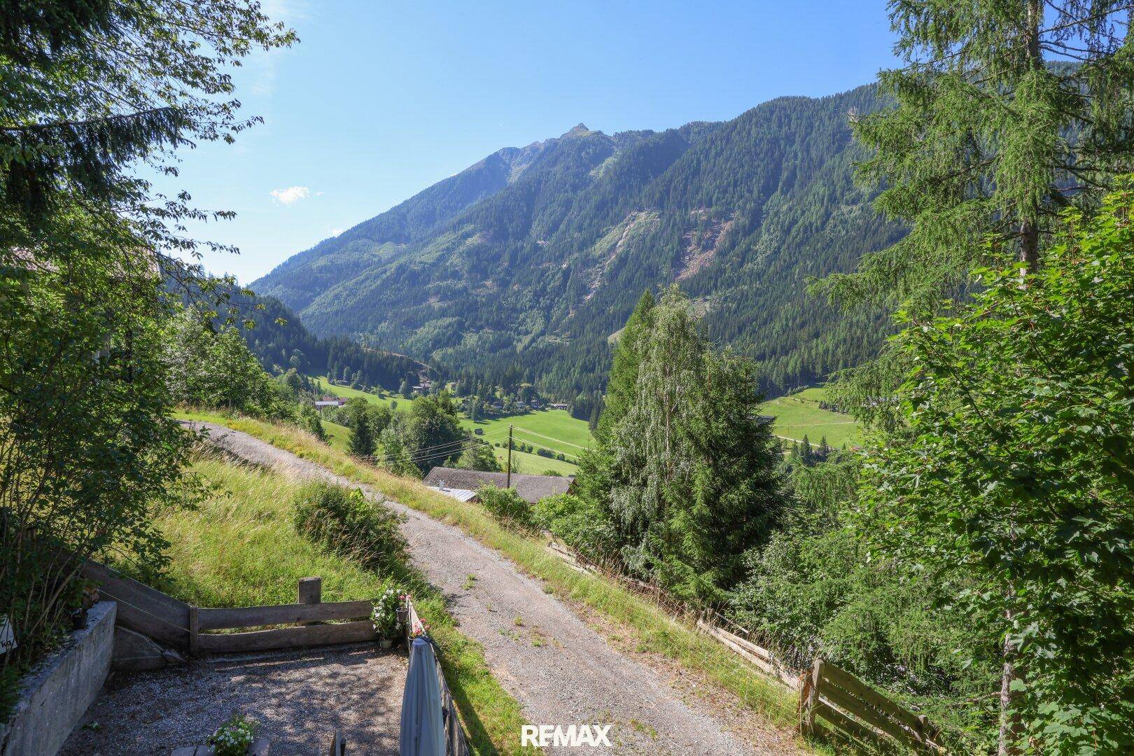 Idyllischer Feldweg führt durch grüne Wiesen mit beeindruckendem Panoramablick auf die Bergwelt.