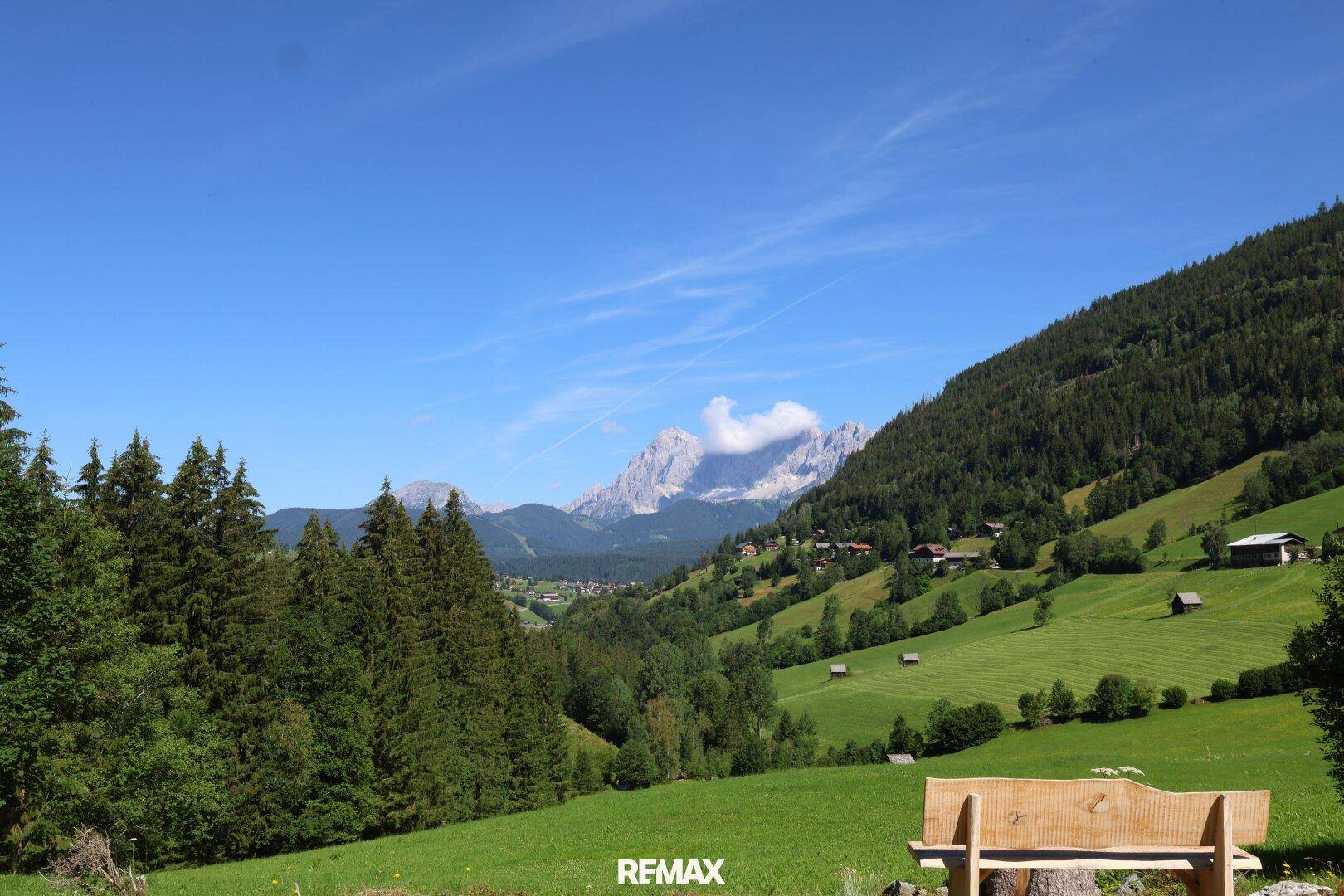 Ruhiger Aussichtspunkt mit Holzbank und weitem Blick über grüne Täler und imposante Berggipfel.