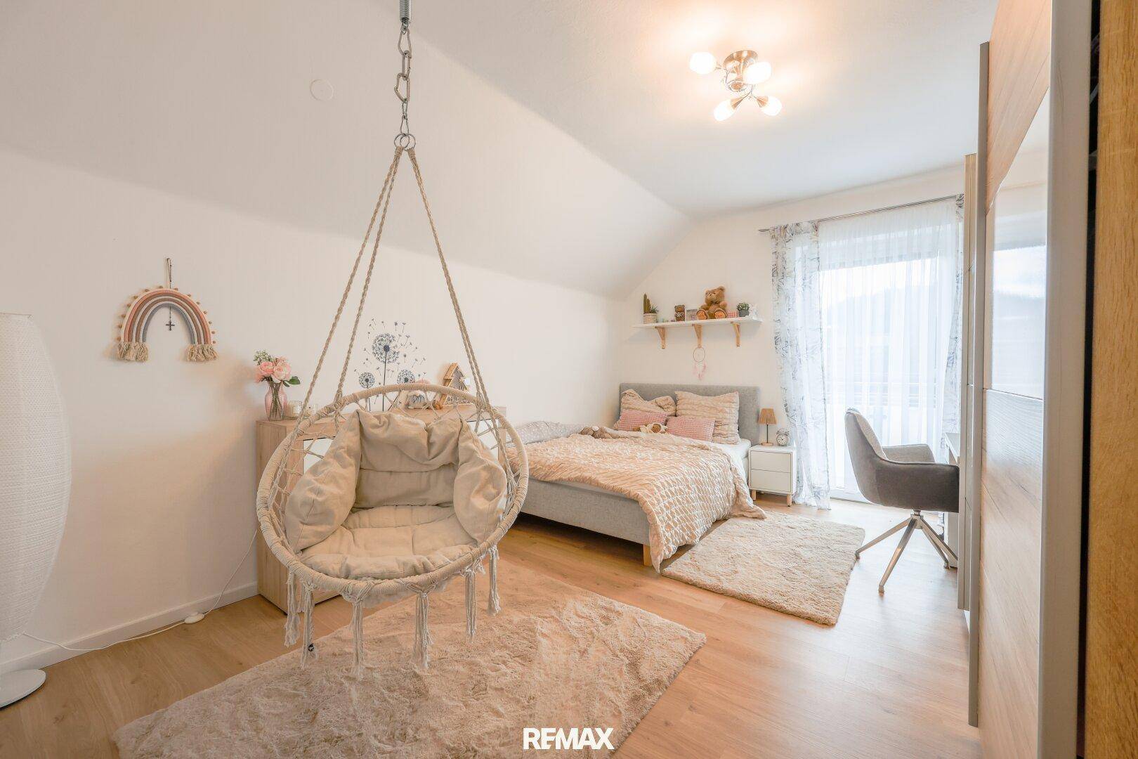 Helles Schlafzimmer mit Holzboden, Hängesessel, Schreibtisch und Zugang zum Balkon.